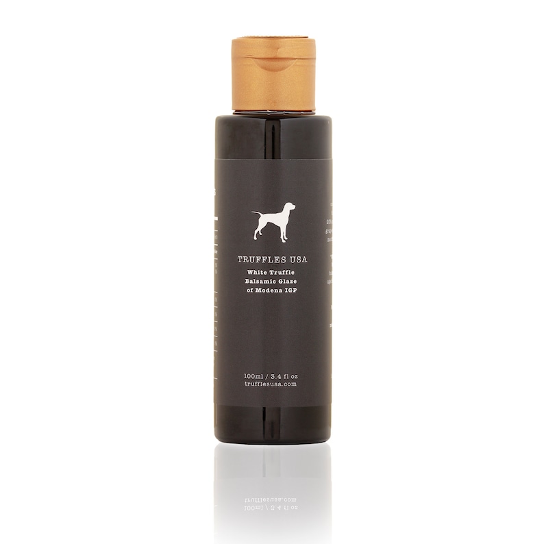 May include: A dark bottle of Truffles USA White Truffle Balsamic Glaze of Modena IGP. The label features a white dog silhouette and product information. The bottle has a gold cap and contains 3.4 fl oz of glaze.