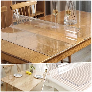 May include: Clear plastic table protector, shown on a wooden table with two glasses of wine. The protector is also shown on a checkered tablecloth.