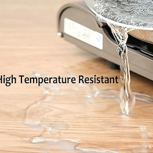 Peut inclure: Gros plan sur un comptoir gris avec de l'eau qui coule d'une casserole en m&eacute;tal. Le texte "High Temperature Resistant" est visible sur l'image.