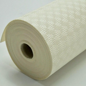 May include: A roll of off-white shelf liner featuring a repeating embossed geometric pattern of concentric octagons. The material is wound tightly around a central cardboard core, displaying a textured surface with a consistent, raised design.