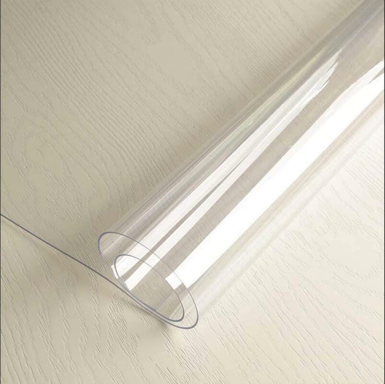 May include: A clear plastic table protector rolled up on a wooden surface.