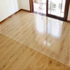 May include: A clear plastic floor protector mat placed on a light brown wood floor. The mat is designed to protect the floor from scratches and damage.