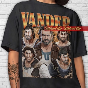 Puede incluir: Camiseta negra con un diseño dorado de "VANDER" y múltiples retratos de un hombre barbudo. El gráfico incluye el texto "LikhenUp". El diseño presenta una estética vintage, con un enfoque en retratos de personajes.