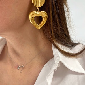 May include: Gold tone heart shaped earrings with a textured round disc at the top.