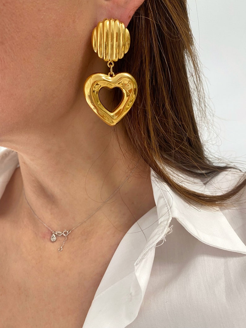 May include: Gold tone heart shaped earrings with a textured round disc at the top.