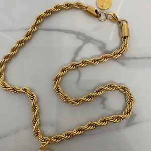 May include: A gold rope chain necklace with a large white pearl pendant. The chain has a lobster clasp and a small round tag with the word "remarkable" on it.