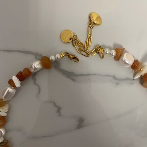 May include: A gold chain necklace with a brown and white stone bead design. The necklace has a small gold charm with the word "Handmade" on it.