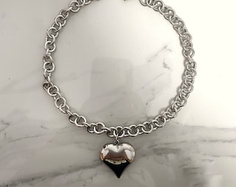 May include: A silver chain necklace with a large, heart-shaped pendant.