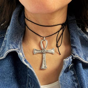 Könnte beinhalten: Eine silberne Ankh-Halskette mit einem schwarzen Choker-Band. Das Ankh ist ein Symbol für Leben und ewiges Leben in der alten ägyptischen Religion.