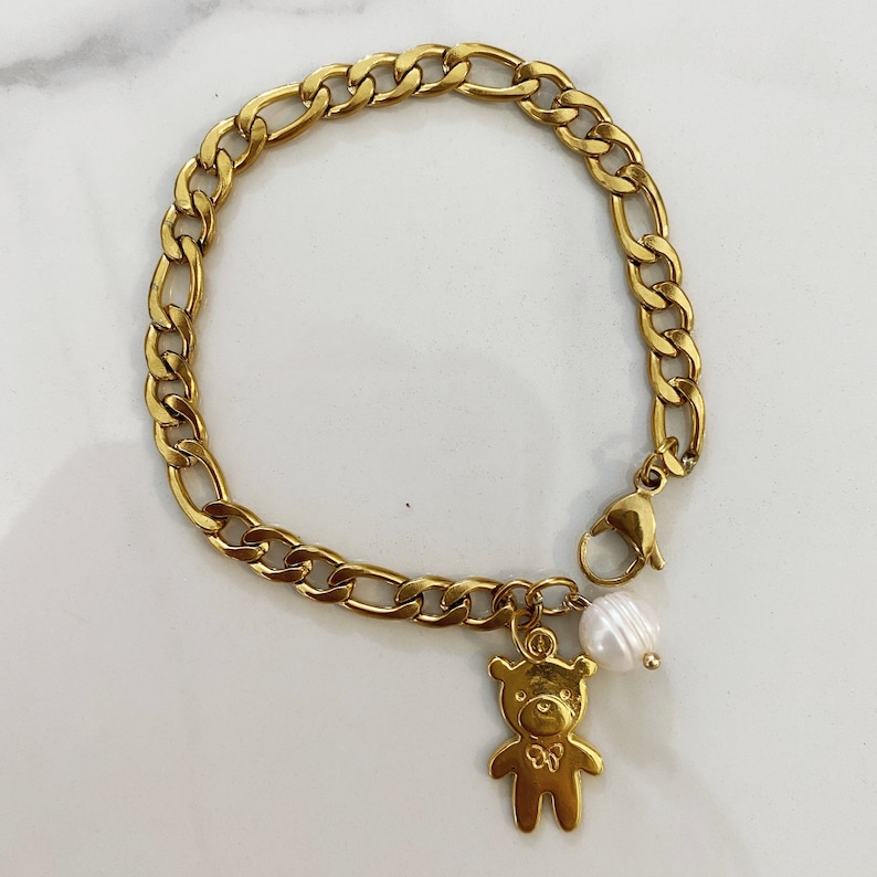 May include: A gold chain bracelet with a charm of a teddy bear and a pearl.