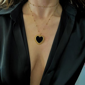 Pu&ograve; includere: Una collana d'oro con un ciondolo a forma di cuore nero. La collana &egrave; composta da due catene sovrapposte.
