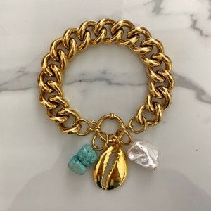 May include: A gold chain bracelet with a large, chunky link design. The bracelet has a charm attached to it, featuring a seashell, a turquoise stone, and a white pearl.