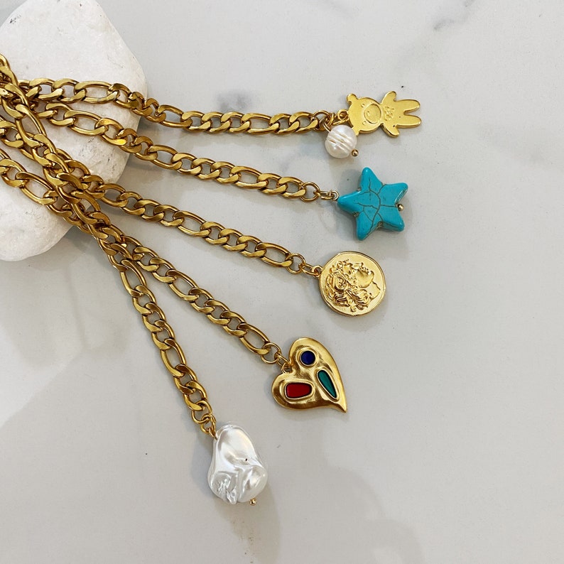 May include: A gold chain necklace with five charms: a pearl, a star with turquoise stones, a coin with a face, a heart with red and blue stones, and a baroque pearl.