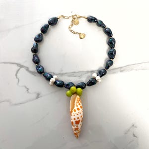 May include: A black pearl necklace with a shell pendant. The shell is orange and white with green accents. The necklace is made of black pearls and gold chain.