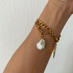 May include: A gold chain bracelet with a large white pearl charm. The bracelet is layered with two different chain styles.