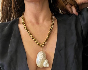 May include: A gold chain necklace with a large white seashell pendant.