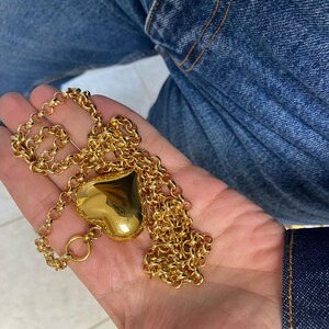 May include: A gold chain necklace with a large, heart-shaped pendant.