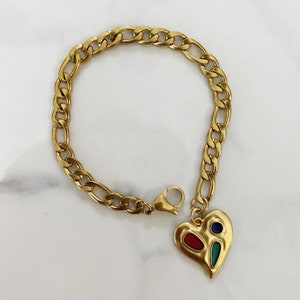 May include: A gold chain bracelet with a heart-shaped charm. The charm is decorated with red, blue, and green enamel.