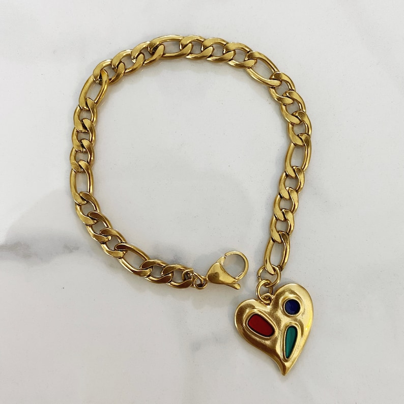 May include: A gold chain bracelet with a heart-shaped charm. The charm is decorated with red, blue, and green enamel.