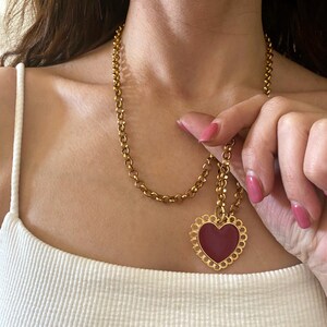 May include: A gold chain necklace with a large, red heart pendant. The heart has a delicate, ornate border.