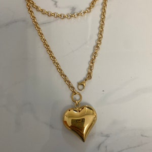 May include: A gold chain necklace with a large, heart-shaped pendant.