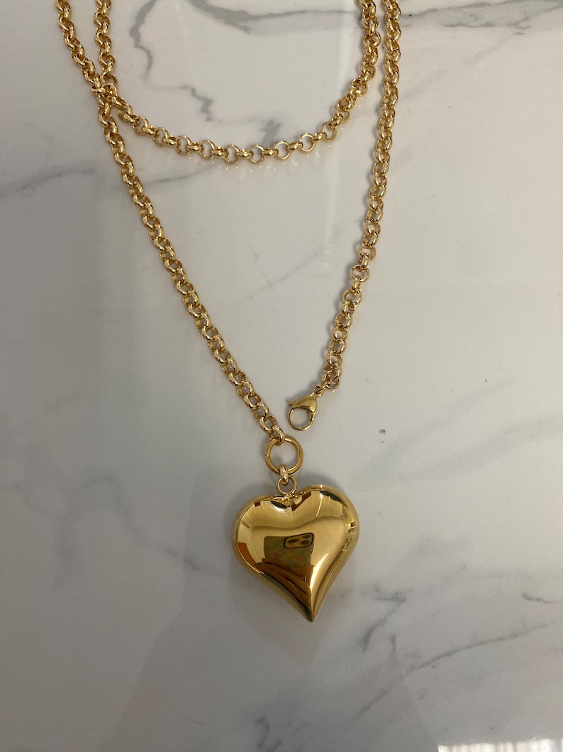 May include: A gold chain necklace with a large, heart-shaped pendant.