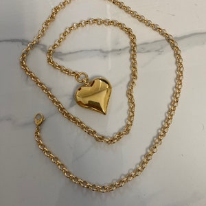 May include: A gold chain necklace with a large, heart-shaped pendant. The chain is a delicate, cable style.