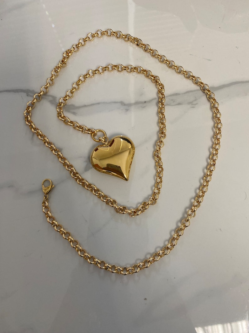 May include: A gold chain necklace with a large, heart-shaped pendant. The chain is a delicate, cable style.