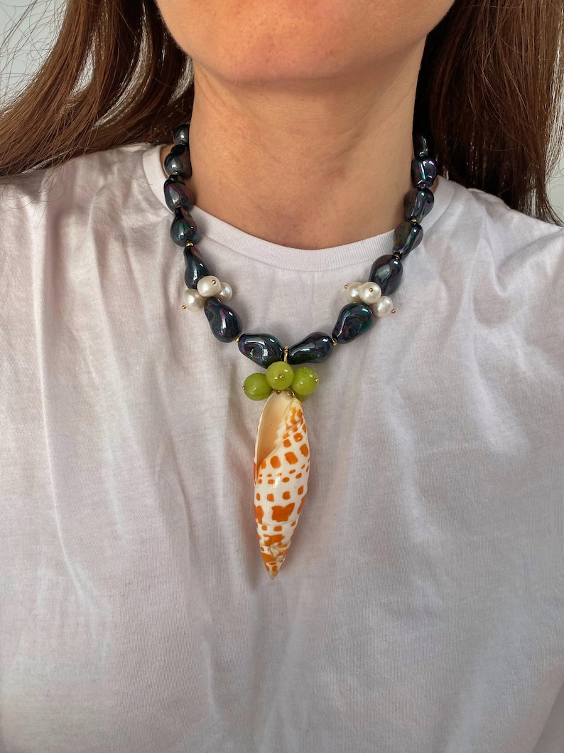 May include: A black and iridescent pearl necklace with a shell pendant. The shell is orange and white with brown spots and is surrounded by green beads.