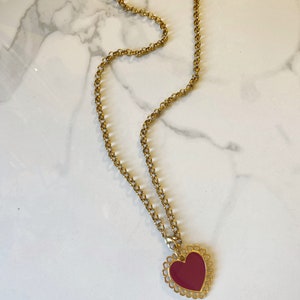 May include: A gold chain necklace with a red heart pendant. The heart has a decorative gold border.