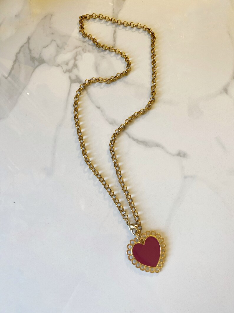 May include: A gold chain necklace with a red heart pendant. The heart has a decorative gold border.