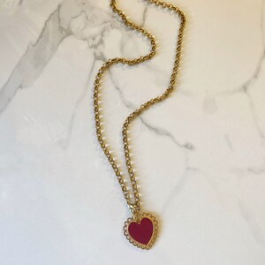 May include: A gold chain necklace with a red heart pendant. The heart has a decorative, scalloped edge.
