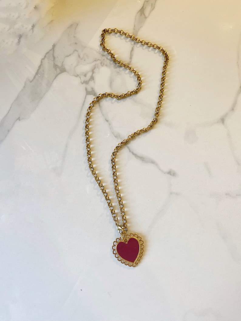 May include: A gold chain necklace with a red heart pendant. The heart has a decorative, scalloped edge.