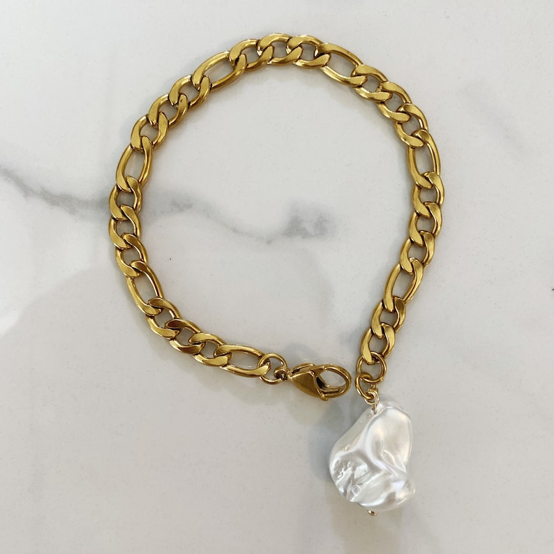 May include: A gold chain bracelet with a large, white, irregular pearl charm.