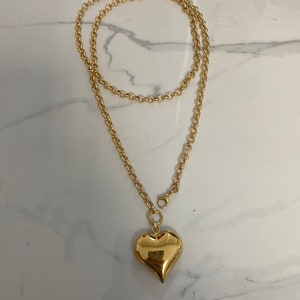 May include: A gold chain necklace with a large, heart-shaped pendant.