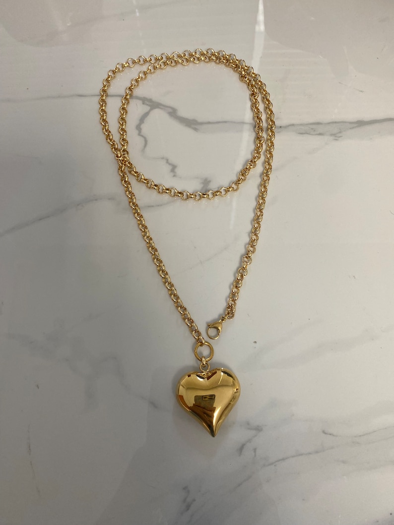 May include: A gold chain necklace with a large, heart-shaped pendant.