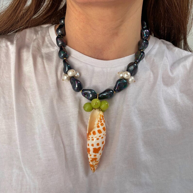 May include: A black and white pearl necklace with a seashell pendant. The seashell is orange and white with a green grape cluster at the top.
