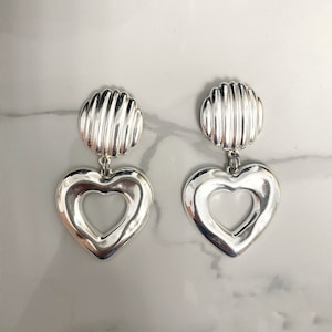 May include: A pair of silver heart-shaped earrings with a textured round disc at the top.