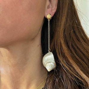 Op de afbeelding: Gouden kettingoorbellen met een witte schelp hanger. De schelp is versierd met witte en bruine strepen.