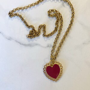 May include: A gold chain necklace with a red heart pendant. The heart has a decorative gold border.