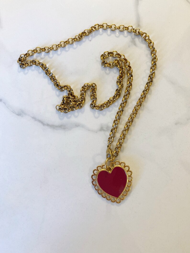 May include: A gold chain necklace with a red heart pendant. The heart has a decorative gold border.