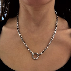 Könnte beinhalten: Eine silberfarbene Halskette mit einem kreisförmigen Anhänger. Die Halskette besteht aus einer Reihe kleiner, abgerundeter Glieder. Der Anhänger ist ein einfacher, polierter Ring. Die Halskette wird um den Hals getragen.