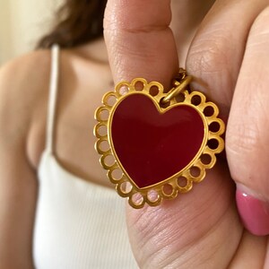 May include: A gold heart-shaped pendant with a red enamel centre and a decorative border of circles.