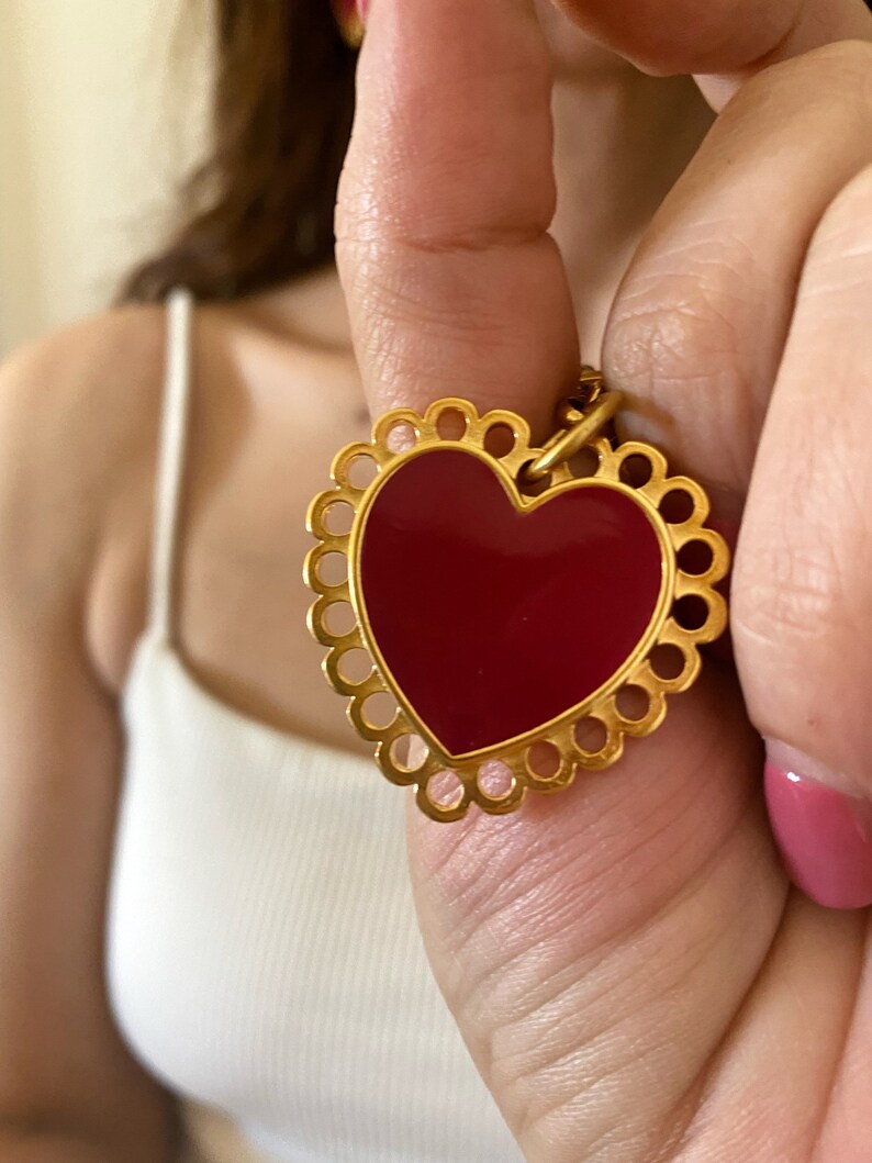 May include: A gold heart-shaped pendant with a red enamel centre and a decorative border of circles.