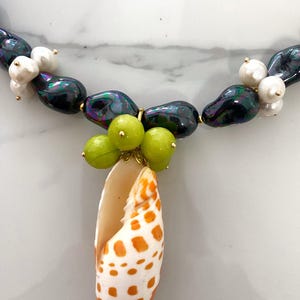 May include: A necklace made of iridescent black beads and white pearls with a shell pendant and green beads.