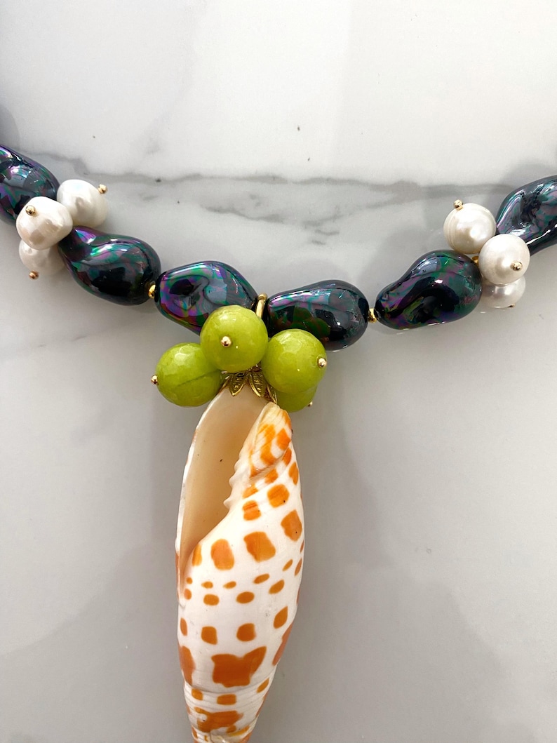 May include: A necklace made of iridescent black beads and white pearls with a shell pendant and green beads.