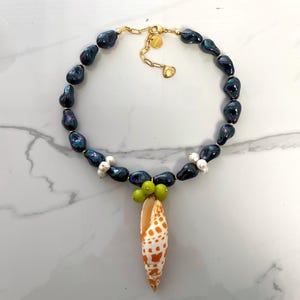 May include: A black pearl necklace with a shell pendant and green beads. The shell is orange and white with a spotted pattern.