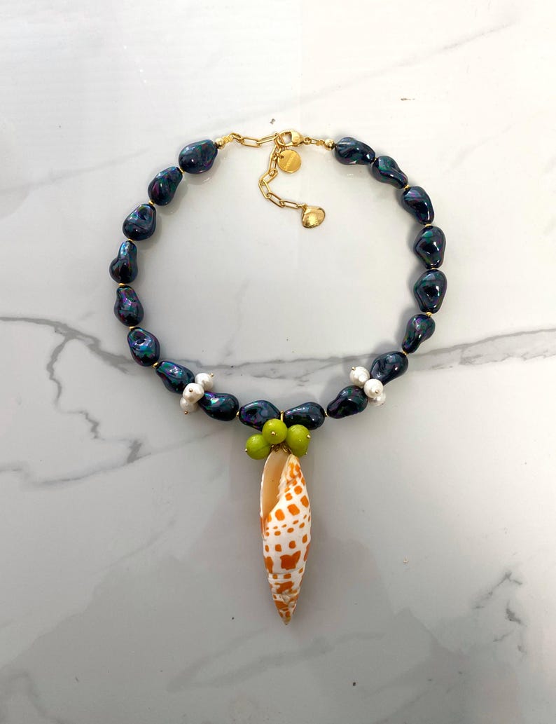 May include: A black pearl necklace with a shell pendant and green beads. The shell is orange and white with a spotted pattern.