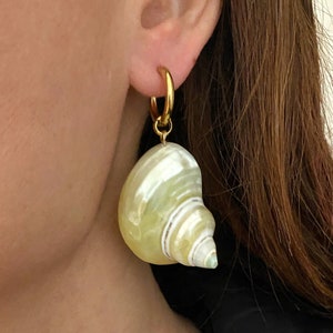 Peut inclure: Boucles d'oreilles créoles dorées avec un grand charme de coquillage blanc et jaune.