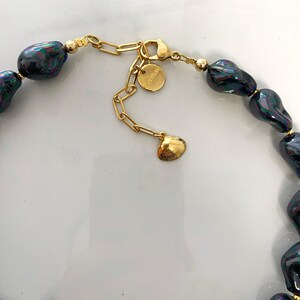 May include: A gold chain necklace with a black baroque pearl pendant. The chain has a lobster clasp and a small charm with the word "Madewell" on it.